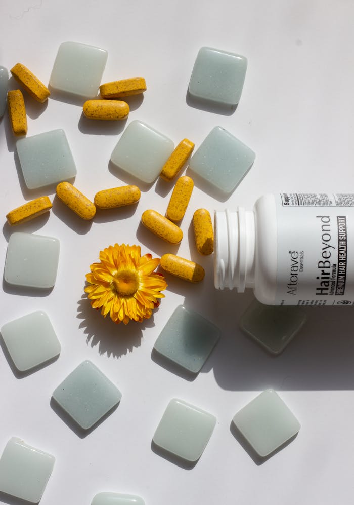 Hair vitamins beside a marigold flower on a white background.