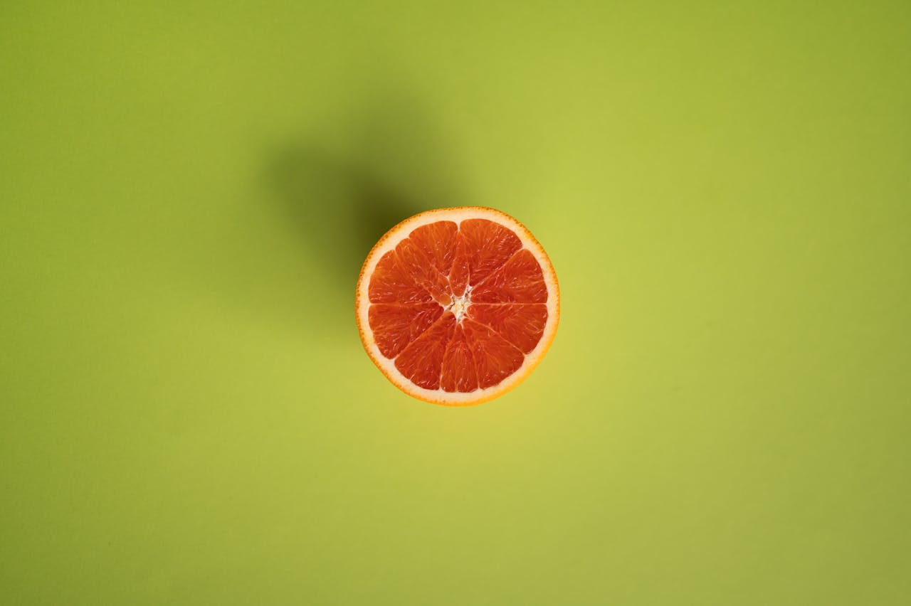 Top view of a fresh grapefruit slice on a vibrant green background, perfect for health and wellness themes.